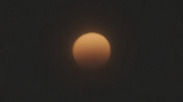 A soft, blurred amber glow dissolving into the dark, its edges lost — a vague, rounded estimate.